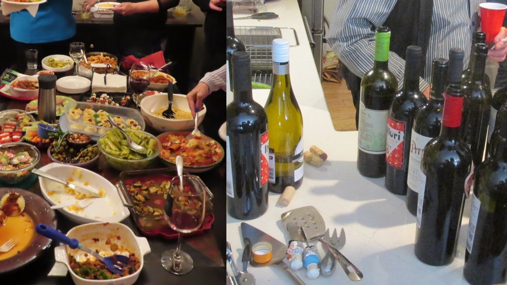GVL A table filled with various dishes, bowls of food, and glasses of wine on the left. On the right, several wine bottles, bottle openers, and corks are placed on a counter. People are serving themselves and mingling in the background.