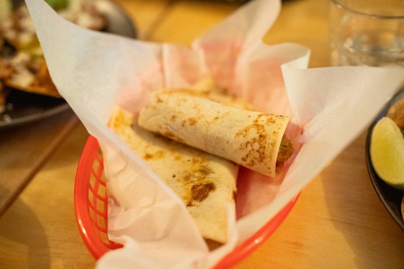 GVL A red basket lined with white paper holds two folded tortillas filled with delectable Honduran ingredients, set on a wooden table. This culinary delight could easily rival any dish crafted by a Shukette Alum in Jersey City.