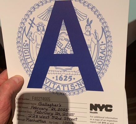 GVL A person holds a sanitary inspection grade card proudly displaying an A Rating. The card details Gallaghers Steakhouse in Manhattan, with an inspection date of February 24, 2023. The NYC Health logo stands out prominently.
