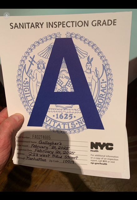 GVL A person holds a sanitary inspection grade card proudly displaying an A Rating. The card details Gallaghers Steakhouse in Manhattan, with an inspection date of February 24, 2023. The NYC Health logo stands out prominently.