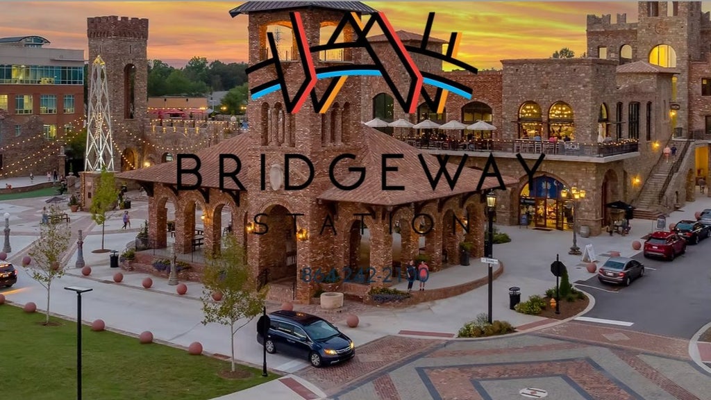 GVL Scenic view of a bustling plaza at sunset, featuring stone buildings with arched pathways. A logo for Bridgeway Station overlays the image. The area is lively with people, string lights, and parked cars.