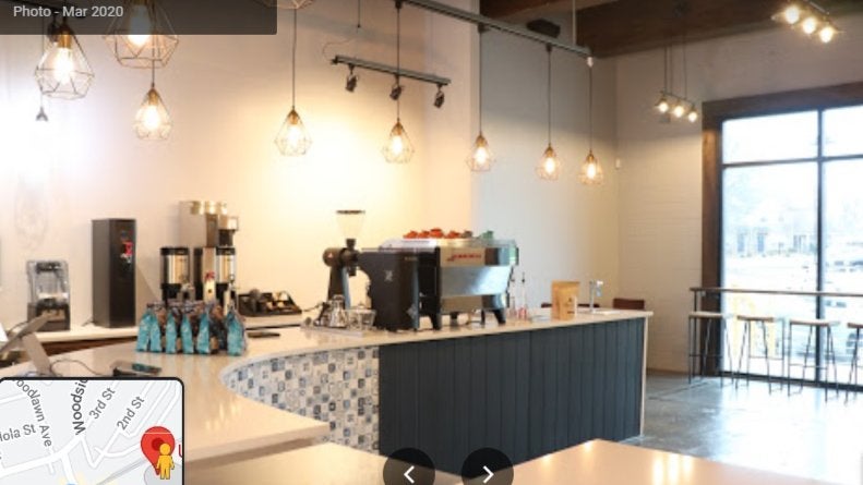 GVL A modern coffee shop interior featuring a central counter with a large espresso machine, coffee bean bags, and equipment. Stylish pendant lights hang from the ceiling. A map snippet is visible in the corner.