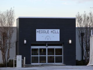 GVL The entrance to a modern building with a sign above the door reading Heddle Hill; bare trees flank the sides and the ground is lightly dusted with snow, as part of Greenville Countys recent Planning Commission review.
