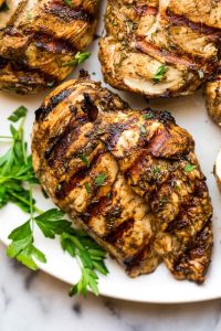GVL Grilled chicken breast with dark grill marks, marinated in a tangy balsamic chicken marinade, garnished with fresh parsley on a white plate. The seasoned chicken looks juicy and flavorful.