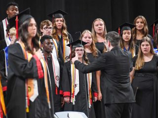 GVL A choir of students in graduation caps and gowns sings as a conductor leads them. The Class of 2025, from Blue Ridge, includes both male and female students, with one standing proudly with a hand over their heart.
