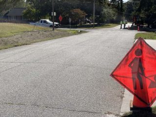 GVL A red construction sign with a person holding a flag stands near the edge of a residential street in Greenville County, where road work—possibly supported by recent road funding—appears to be taking place further down the road.