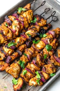 GVL Grilled Chicken Kebab skewers with marinated chicken and red onion, garnished with fresh cilantro and served on a metal tray.