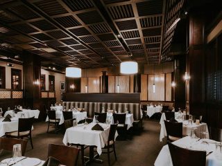 GVL Elegant restaurant interior with dark wood accents, white tablecloths, and cushioned chairs sets the stage at Rick Erwin’s West End. Pendant lights create a warm, sophisticated ambiance in the dining room, ready for guests featured in this Weekly Dish.