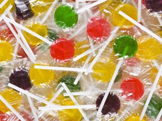 GVL A pile of colorful lollipops, including red, green, yellow, and purple, individually wrapped in clear plastic with white sticks—sweet enough to headline a weird news segment in News of the Weird.