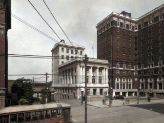 GVL A historic street scene shows an old-fashioned streetcar at a downtown Greenville intersection, with large brick and white stone buildings, including the famed Westin Poinsett, a notable Greenville landmark, and overhead electrical wires visible.