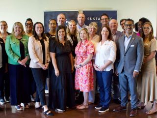 GVL A group of Upstate residents, both men and women, stand together indoors, smiling at the camera. Dressed in business casual attire, they gather in front of a banner for the Sustainability Leadership Initiative as 2025 graduate candidates.