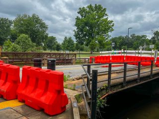 GVL Bright orange barricades block the South Hudson Street bridge in Greenville, signaling a bridge replacement and preventing access to the road. Trees and grassy areas appear in the background beneath a cloudy sky.