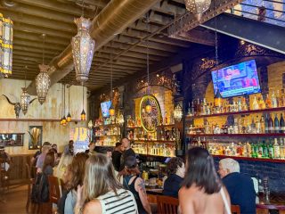 GVL People sit at The Matador’s busy bar, surrounded by ornate lights, exposed beams, and sports on TV—a lively, rustic spot rumored for extended hours after a Greenville Board of Zoning Appeals decision.