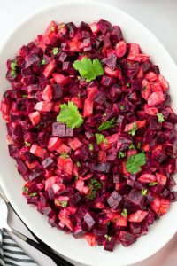 GVL A white oval plate filled with a vibrant potato salad of diced beets and potatoes, garnished with fresh cilantro leaves. This summer favorite features colorful cubes mixed evenly for a bright, appetizing presentation.