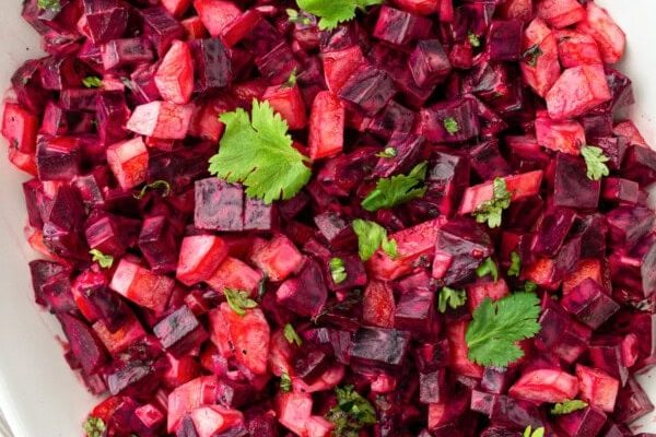 Better Than Potato Salad? This Creamy Beet Side Is a Summer Favorite GVL A white oval plate filled with a vibrant potato salad of diced beets and potatoes, garnished with fresh cilantro leaves. This summer favorite features colorful cubes mixed evenly for a bright, appetizing presentation.