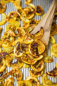 GVL Roasted squash sliced and browned on a baking sheet, with a wooden spatula mixing the crispy pieces—a delicious side dish ready in under 20 minutes.
