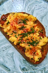 GVL A slice of toasted bread topped with creamy scrambled eggs, inspired by Deviled Egg Toast, sprinkled with chopped herbs, sesame seeds, and a dash of paprika, served on a marbled plate.