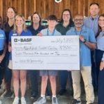 GVL A group of people from BASF SC stand together holding a $7,500 ceremonial check for Make-A-Wish to benefit an Upstate child. They are smiling and posing indoors in front of a wooden wall.