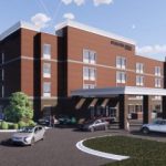GVL A modern, four-story brick building with large windows and a covered entrance stands near the downtown hotel, with cars nearby and landscaped areas in view, capturing the vibrant atmosphere of Fountain Inn.