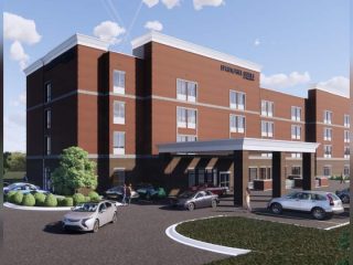 GVL A modern four-story brick building with large windows, labeled HOSPITAL NAME above the entrance, stands in Fountain Inn and features a covered drop-off area where several cars and people are visible in the driveway.